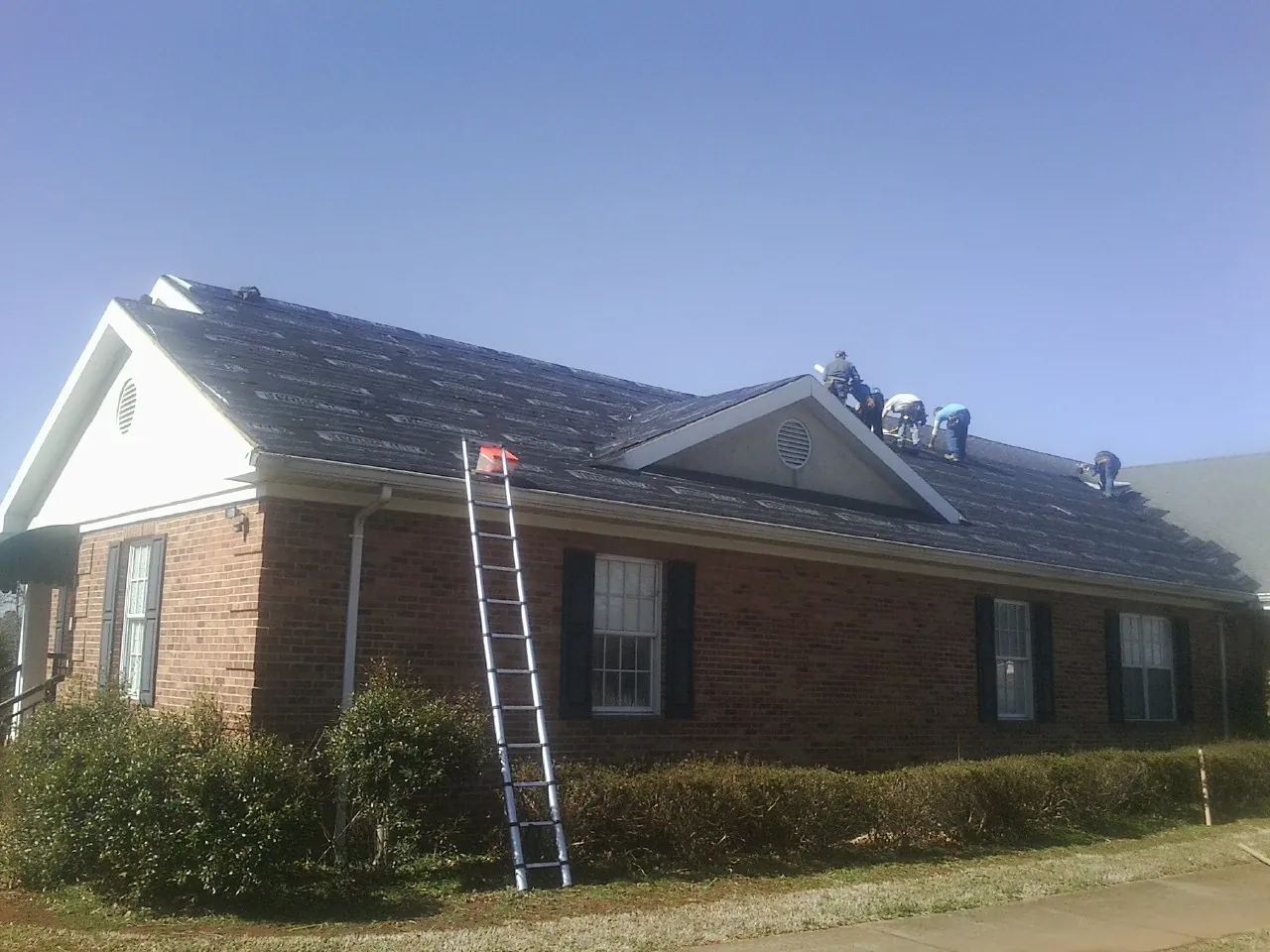 Crew tearing shingles off a brick ranch roof with a ladder set — Metal Roof Repair work by our crew in White City