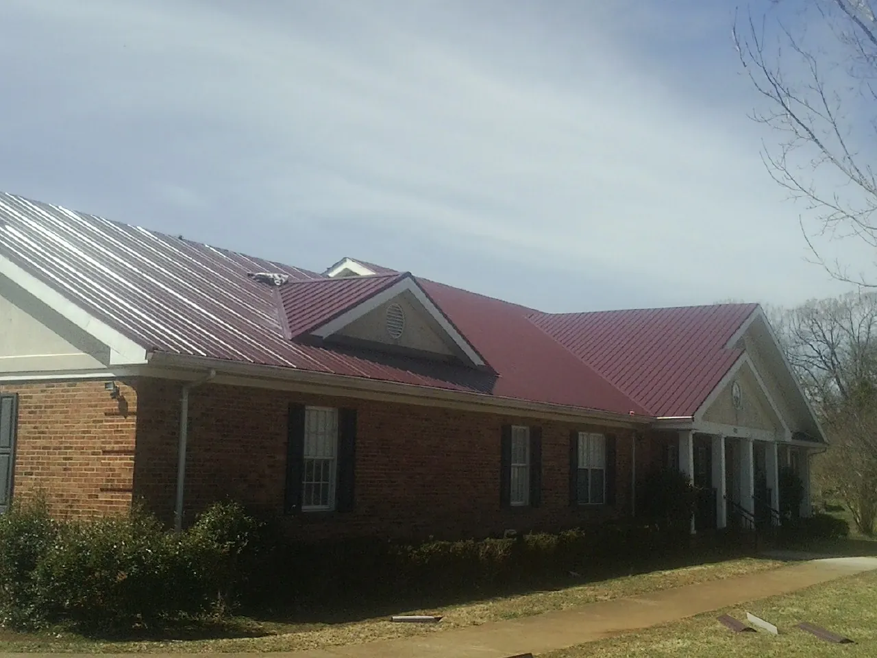 Red metal roof with gabled entries on a long brick building, from a Hail Damage Roof Repair job in White City