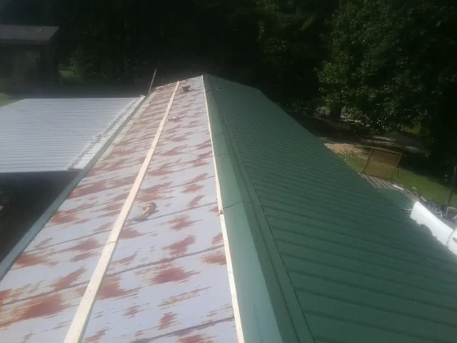 Old rusted panels beside newly installed green metal roofing — Wind Damage Roof Repair by Roofing Brothers in White City