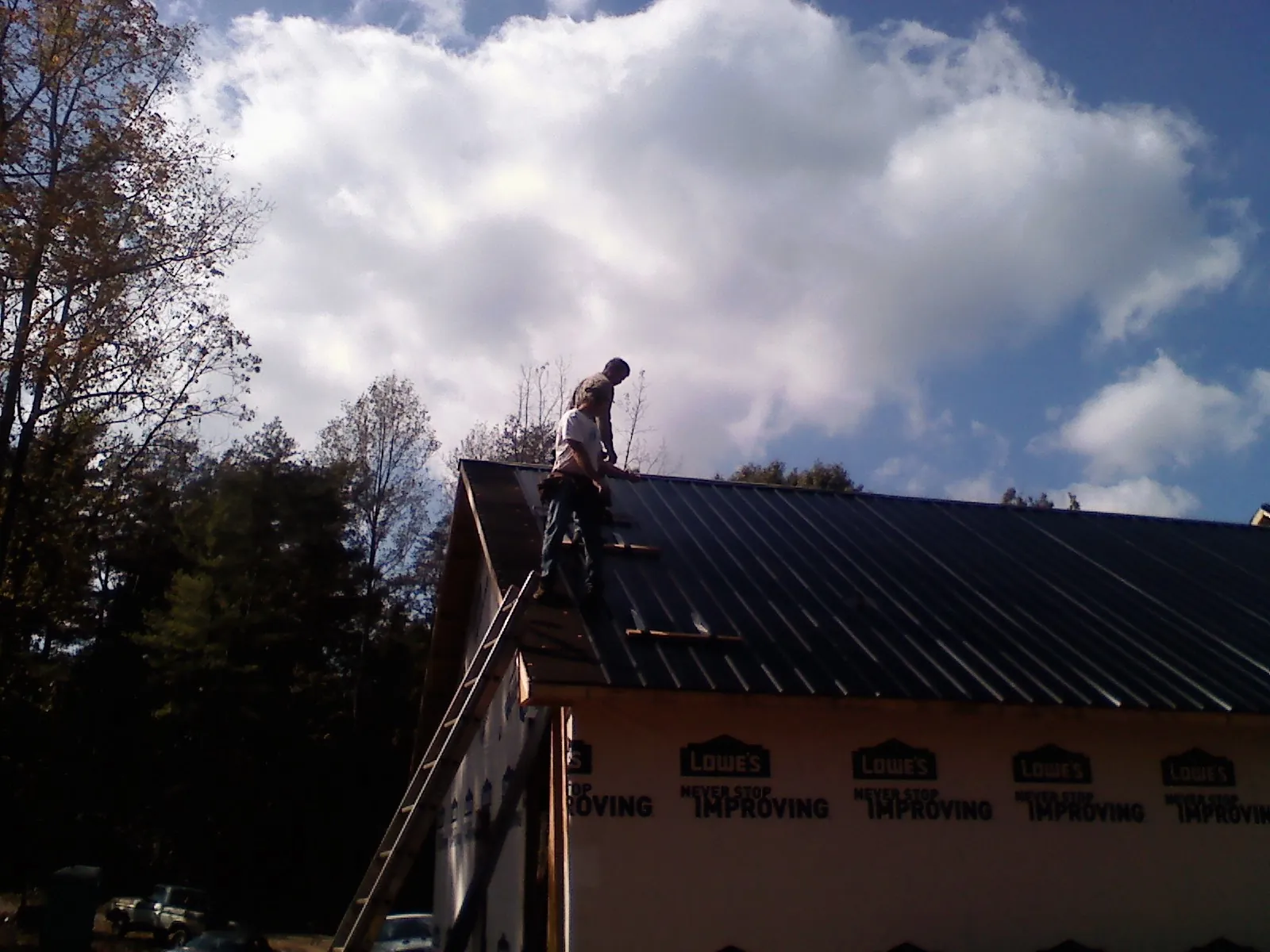 Roofer fastening dark metal panels high against a cloudy sky, from a Roof Inspection job in White City
