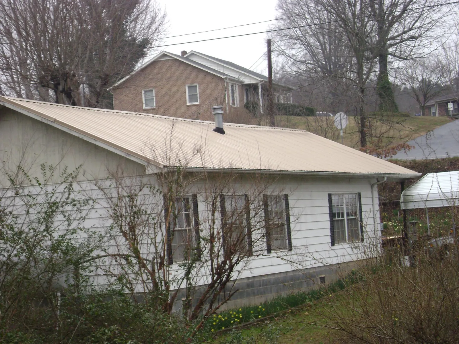 Tan metal roof on a white sided house set into a hillside — Commercial Roofing by Roofing Brothers in White City